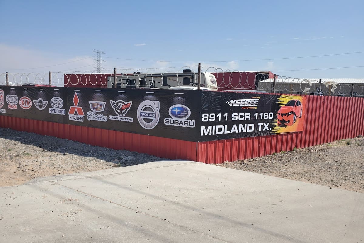 Keesee Auto Parts: Red metal fence topped with razor wire and a banner showing car brand logos and the Midland, TX address