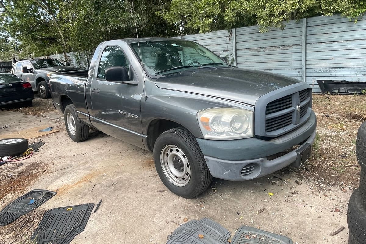 Morgan Salvage: Gray pickup truck parked on a dirt lot beside a fence, with other vehicles, floor mats and tires scattered around