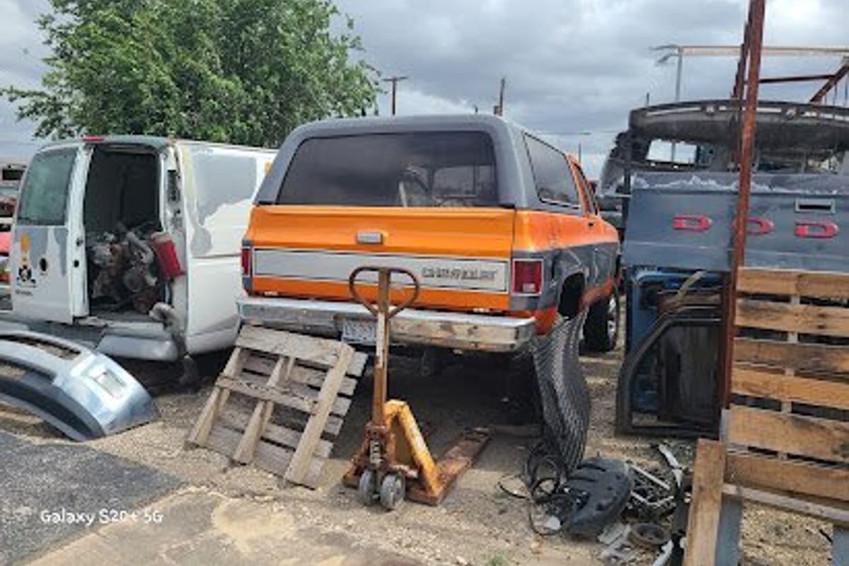 Drive In Truck Salvage: Salvage yard lot with an orange and gray Chevrolet SUV, a white van, wooden pallets and scattered vehicle parts