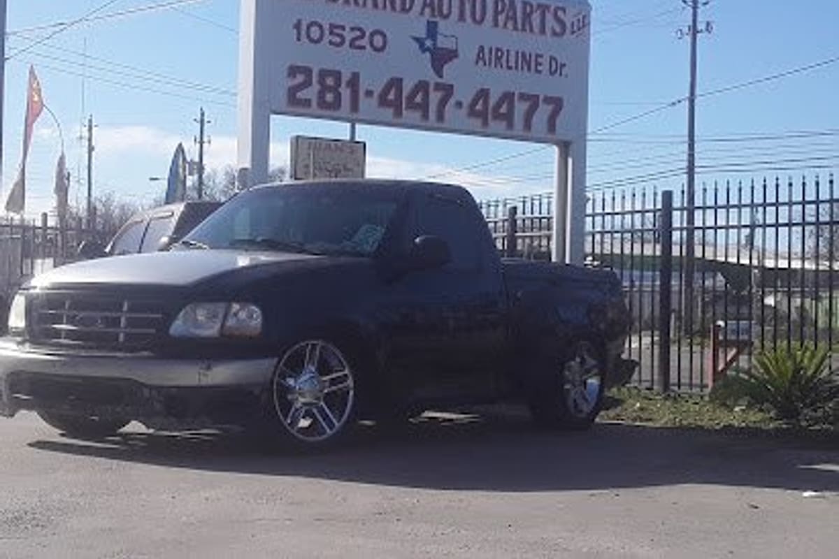 All Brand Auto Parts: Large roadside sign reading All Brand Auto Parts with address and phone number, beside an iron fence and a parked black pickup truck