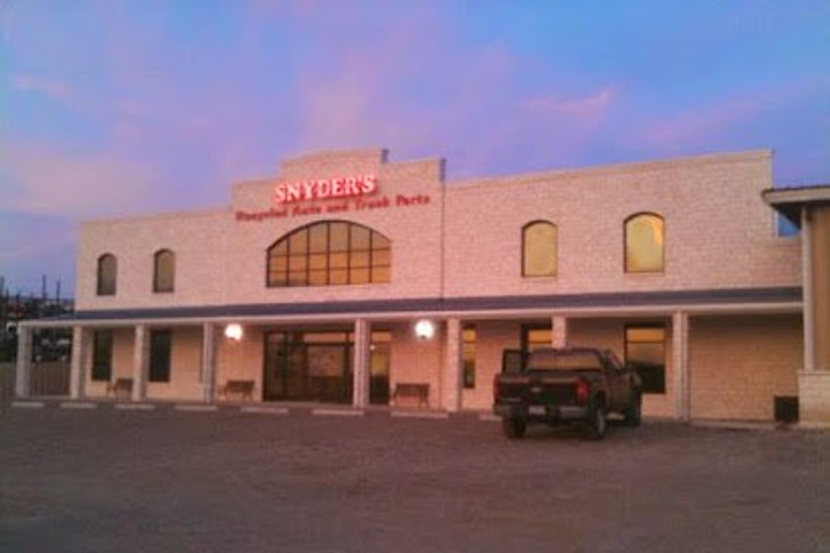 Snyder Salvage: Two-story stone building with a lit red sign above a covered porch, a pickup truck parked in the gravel lot at dusk