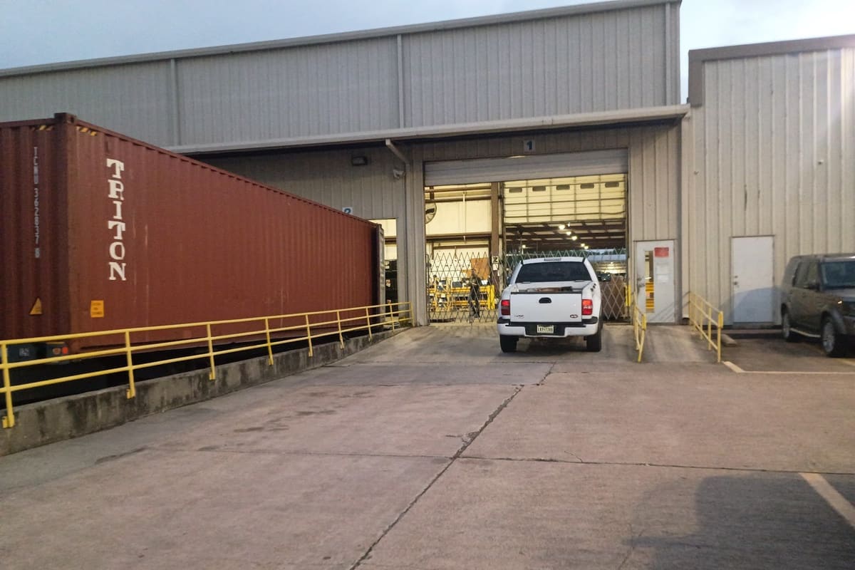 LKQ Best Automotive: Metal warehouse with a loading dock bay, a shipping container beside a yellow railing, and a white pickup parked at the door