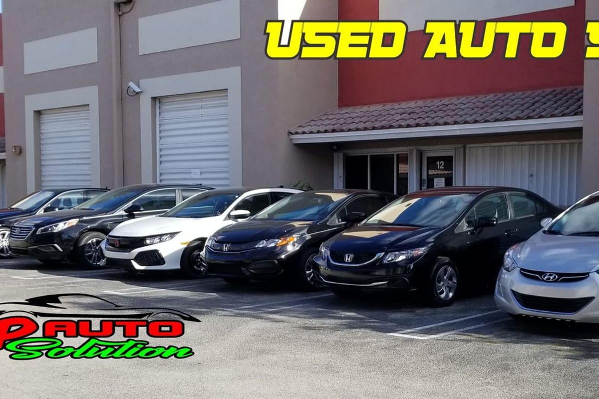 JP Auto Solution: Row of used cars parked in front of a tan and red industrial unit building with roll-up doors