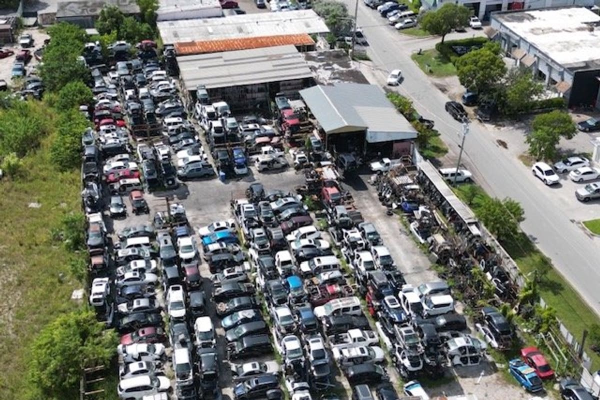 Gardner Auto Parts: Aerial view of a salvage yard with dense rows of parked vehicles beside a street and metal-roofed buildings