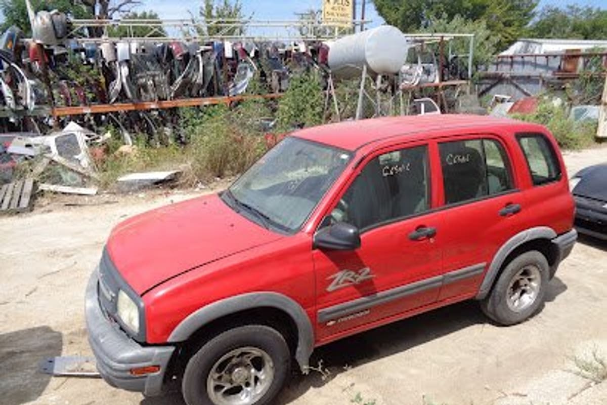 A Plus Auto Salvage: Red SUV parked on a dirt lot in front of racks of salvaged car parts and wrecked vehicles