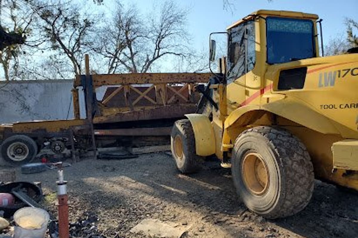 Diaz Garage & Salvage: Yellow wheel loader parked on a gravel salvage yard beside a rusty flatbed trailer and scattered tires and debris