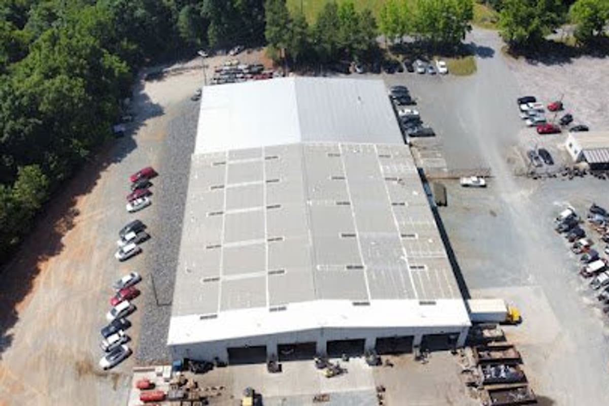 Revolution Auto Parts: Aerial view of a large metal-roofed warehouse surrounded by gravel lots with rows of parked vehicles and trees