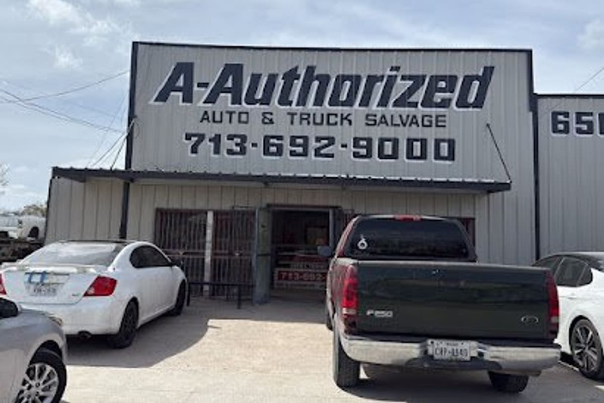 A-Authorize Auto & Truck Salvage: Metal salvage shop building with a large painted sign and phone number, cars parked in front of the entrance