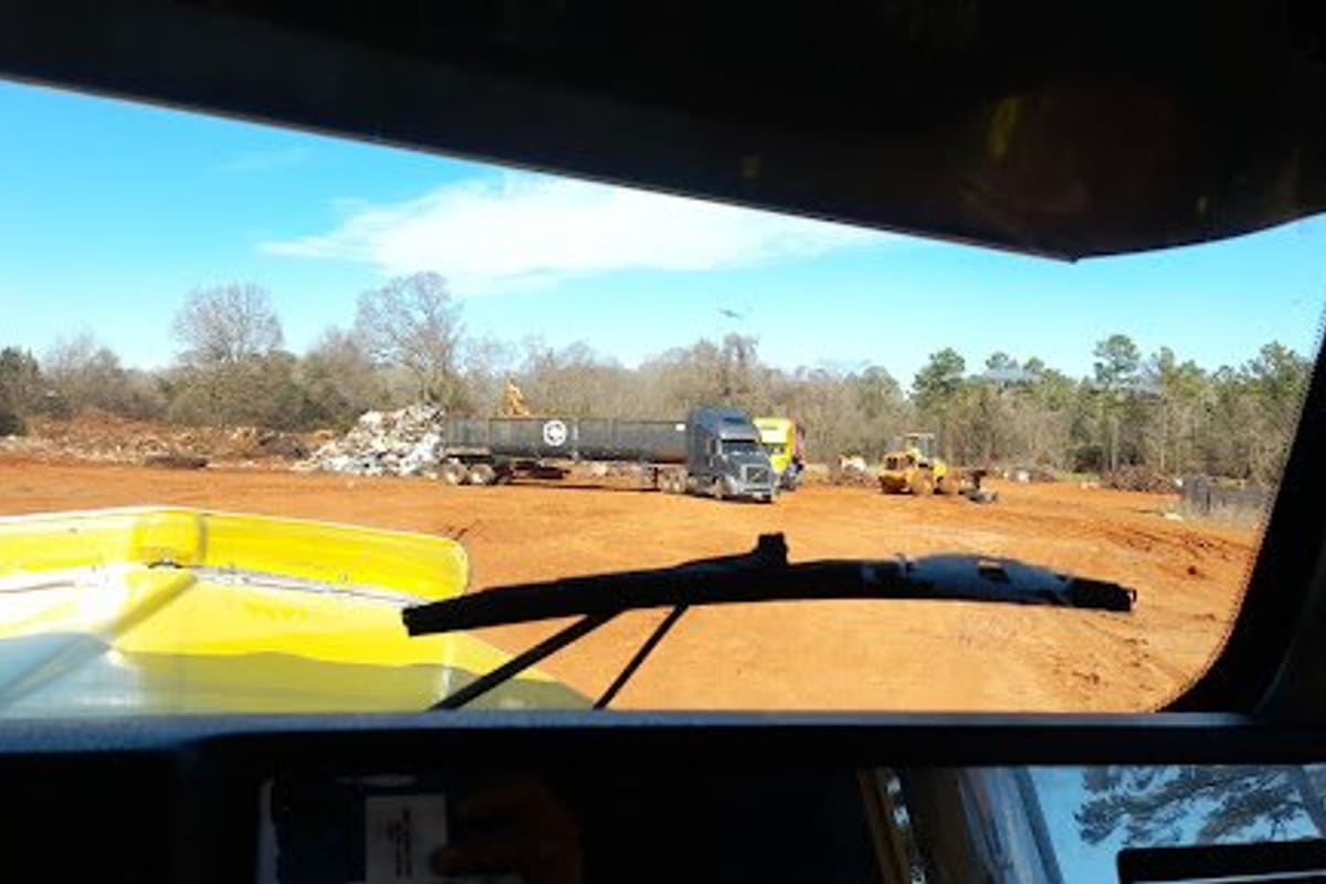 Lane Recyclers: View across a dirt scrap yard with a flatbed truck, loader and piles of scrap metal under a clear sky