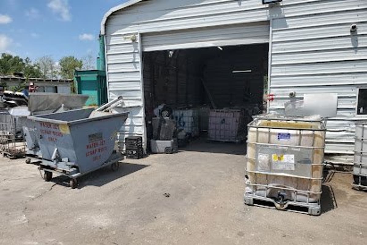 Mohawk Auto Crushing: Metal garage-style building with open bay door, a scrap hopper and a large liquid tote on a paved lot