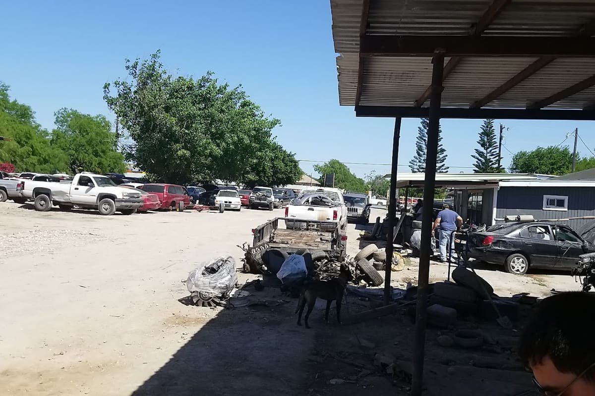 L G Auto Parts: Dirt salvage yard with rows of parked trucks and cars under a covered work area on a sunny day