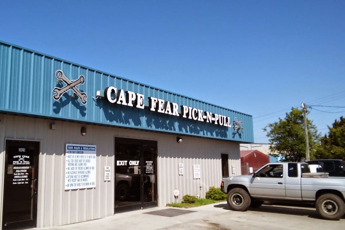Cape Fear Pick N Pull: Metal-sided auto salvage building with a blue upper facade, large lettered sign, entrance doors, posted yard rules and a pickup parked outside