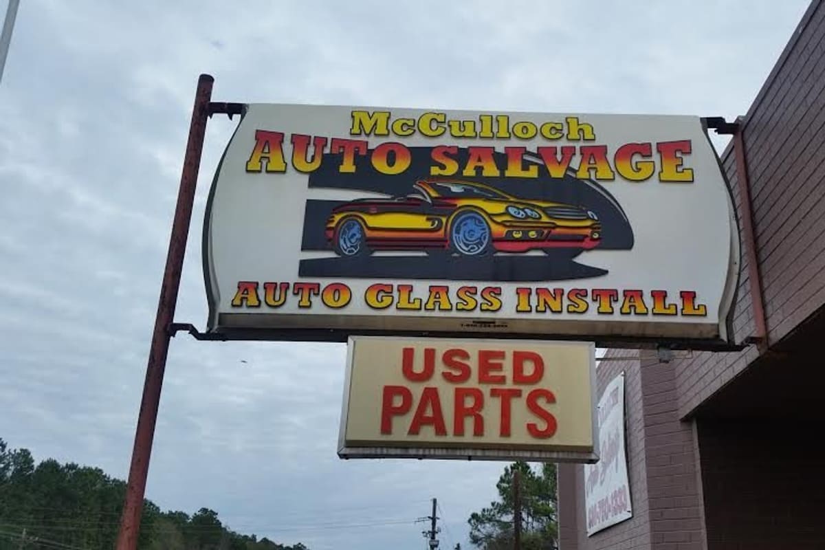 McCulloch Auto Salvage: Hanging roadside sign reading Auto Salvage, Auto Glass Install and Used Parts beside a brick building
