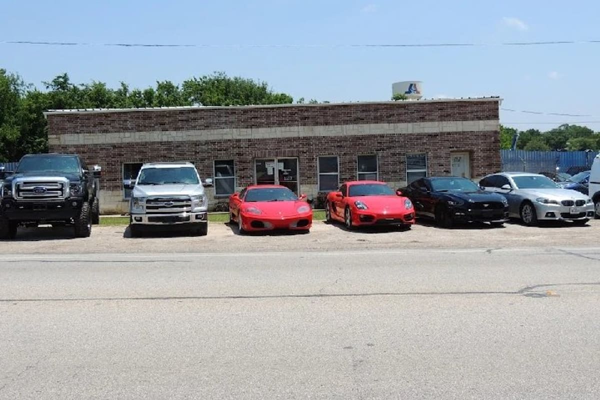 All Star Auto Salvage: Single-story brick building with trucks and sports cars parked in front along a road on a sunny day
