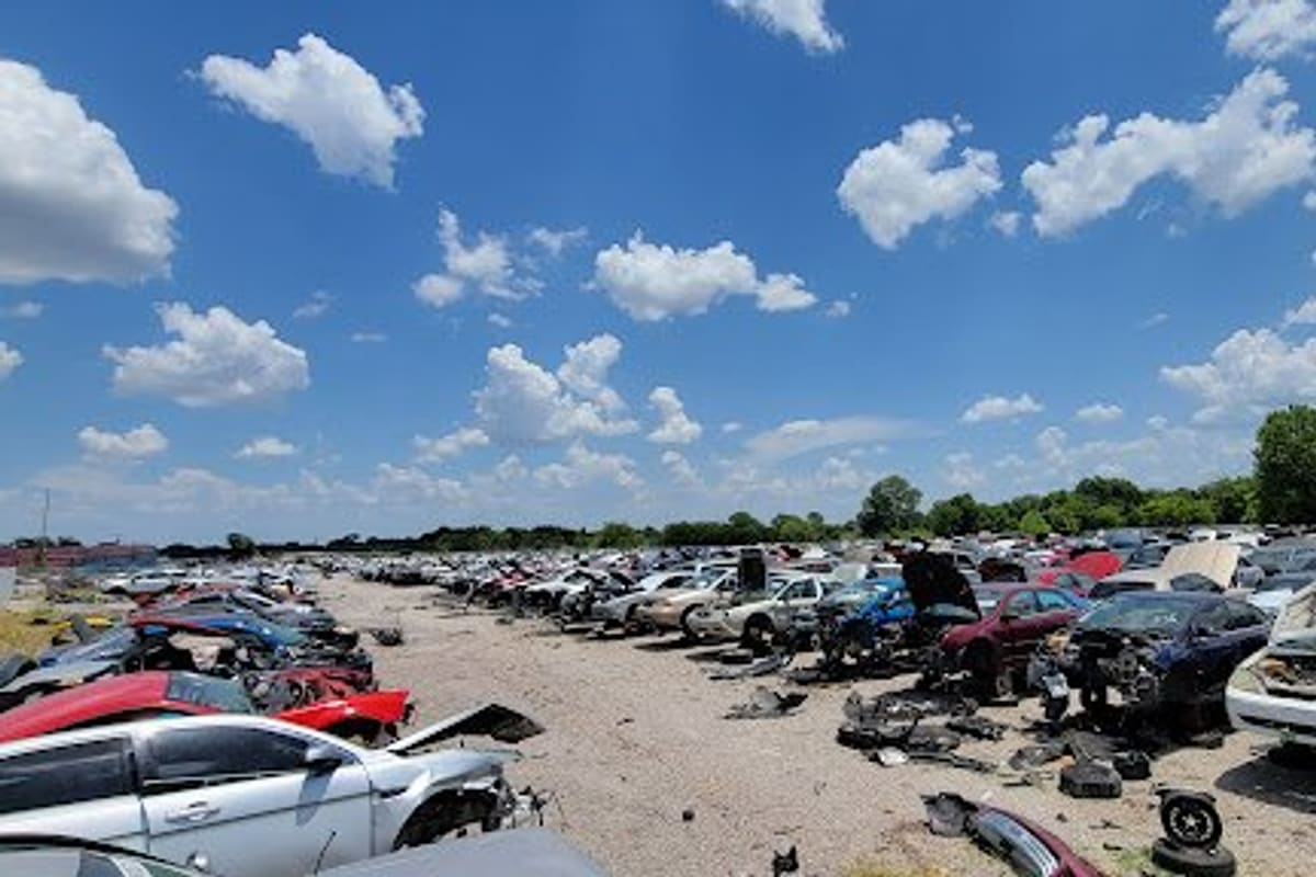 Stop N Pull Auto Parts Salvage: Wide view of a salvage yard with long rows of wrecked cars on a gravel lot under a blue sky with clouds