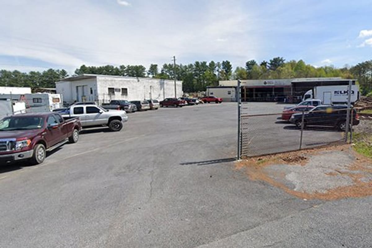 LKQ Bristol TN: Gated entrance to an auto salvage lot with parked trucks, a white building, and a box truck behind a chain-link fence