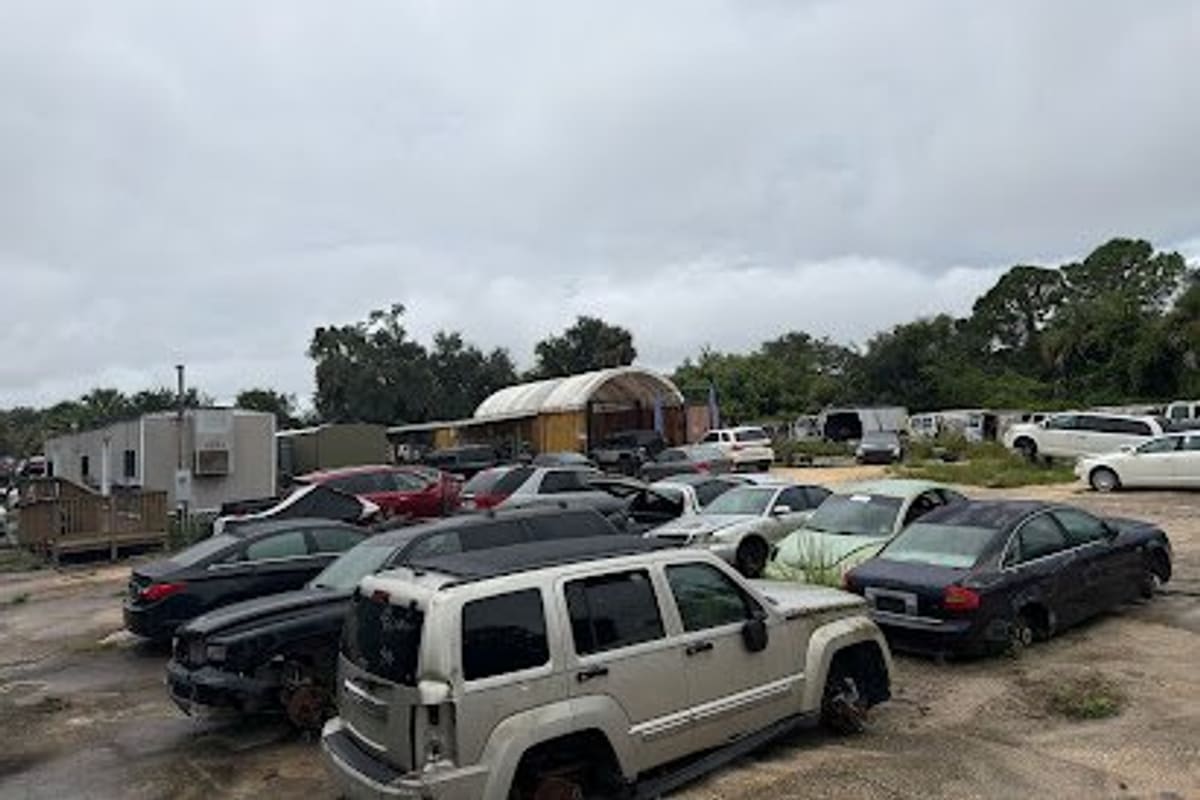 Hibiscus Auto & Salvage: Wide daytime view of a salvage yard with rows of wrecked cars and SUVs, a trailer office and a covered shed in the background