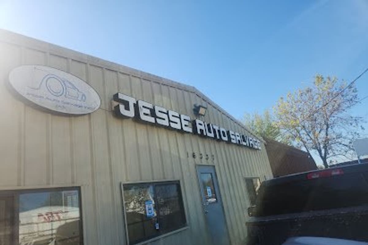 Jesse Auto Salvage: Tan metal office building with large lit block-letter auto salvage sign, entrance door and windows under a clear blue sky