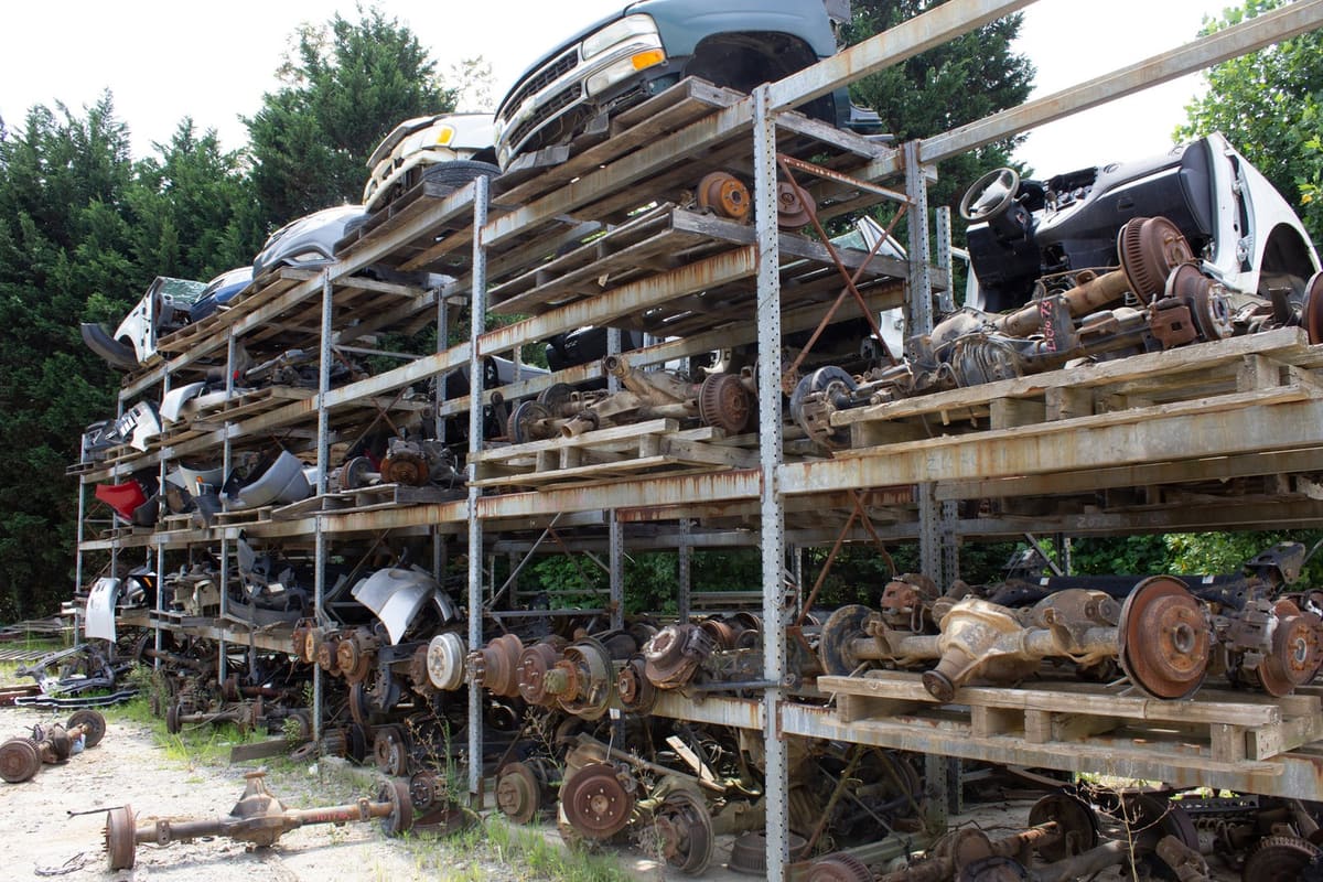 Johnson Auto Recycling: Tall metal racks stacked with car bodies, axles and parts in an outdoor salvage yard with trees behind