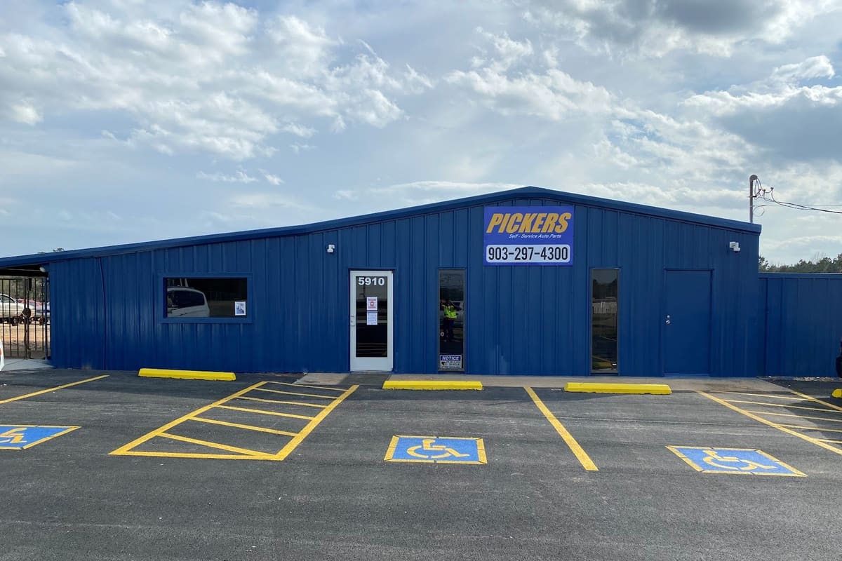 Pickers Self-Service Auto Parts: Blue metal self-service auto parts building with a phone number sign, glass entrance door and handicap parking spaces in front