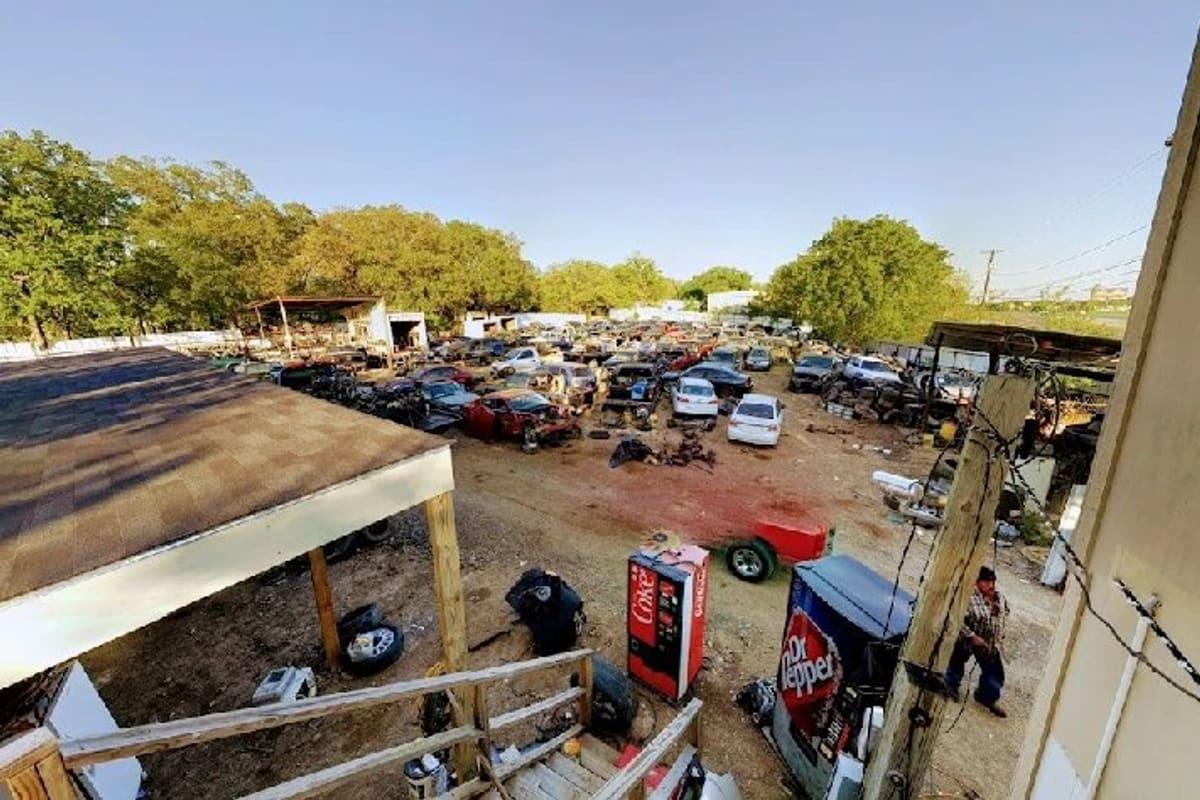 Kleberg Auto Salvage: Elevated view of a salvage yard with rows of wrecked cars, vending machines and a covered shed on dirt ground