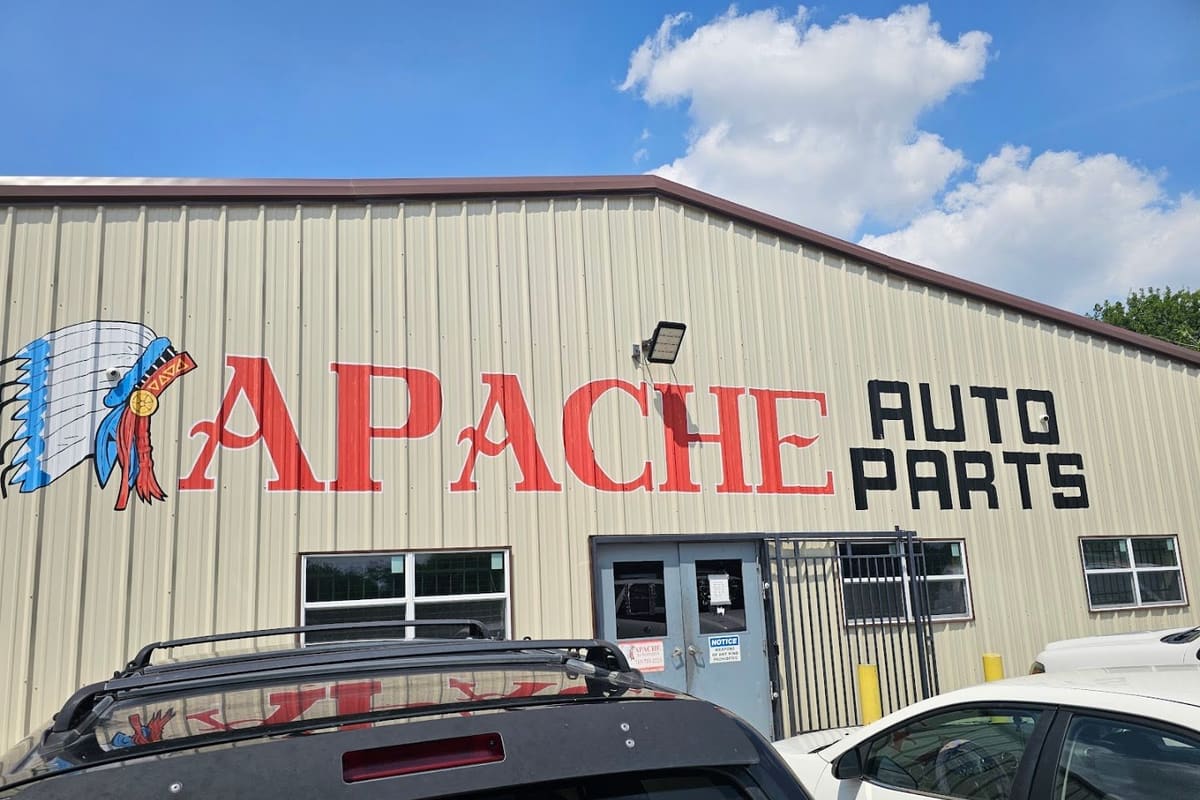 Apache Auto Parts: Tan metal building with a painted Native American headdress and large red and black lettering above a gray double door entrance