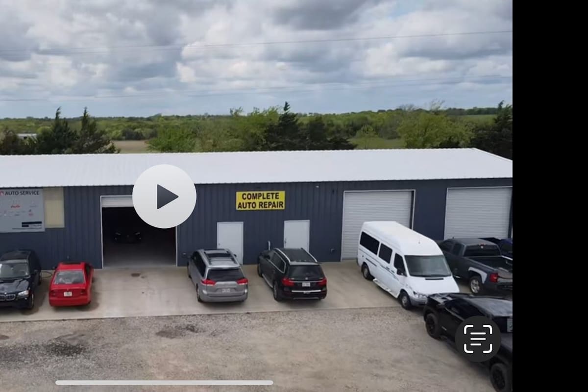 Hi-Q1 Auto Service: Blue metal auto repair shop building with a yellow sign and several cars parked on the concrete apron in front