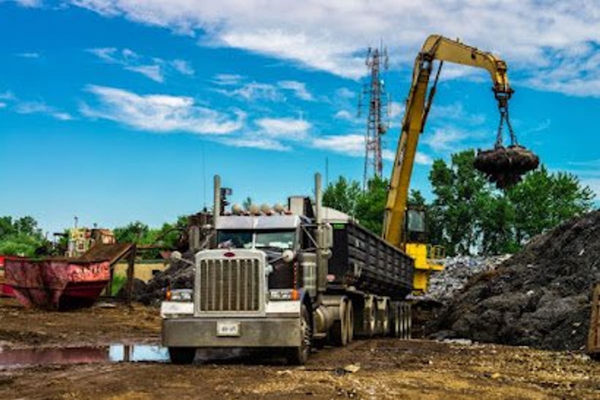P&S Auto Salvage: Dump truck and yellow material handler crane loading scrap beside a large scrap pile in an outdoor salvage yard