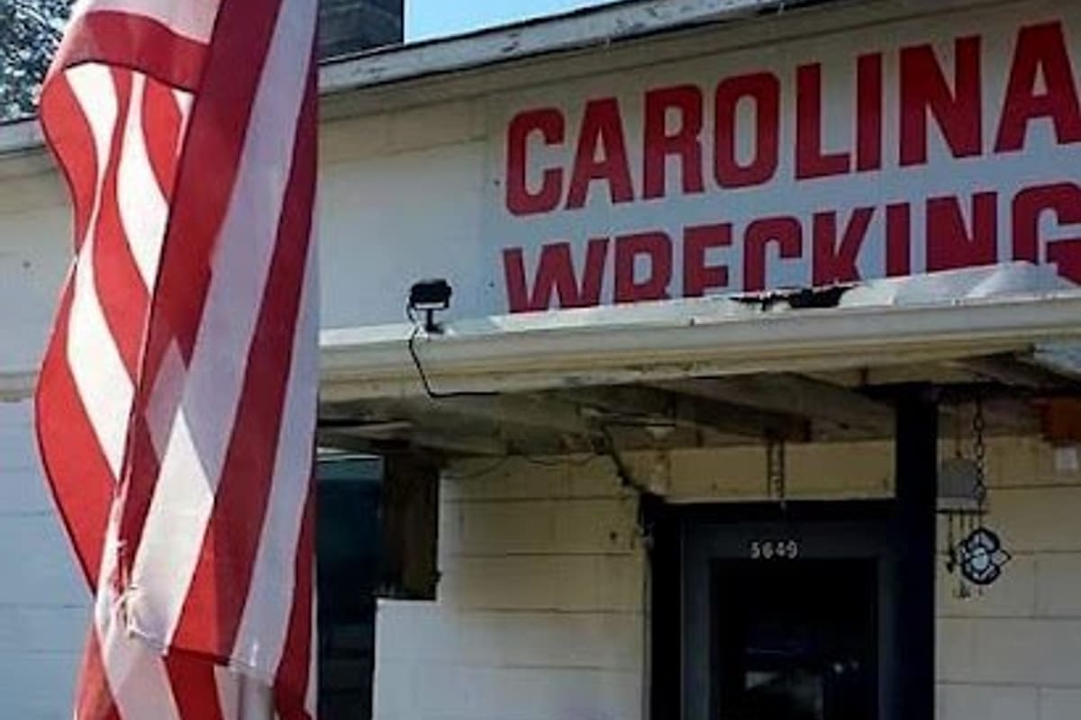 Carolina Wrecking: Single-story white block building with a large red sign and an American flag in the foreground, door marked 5649