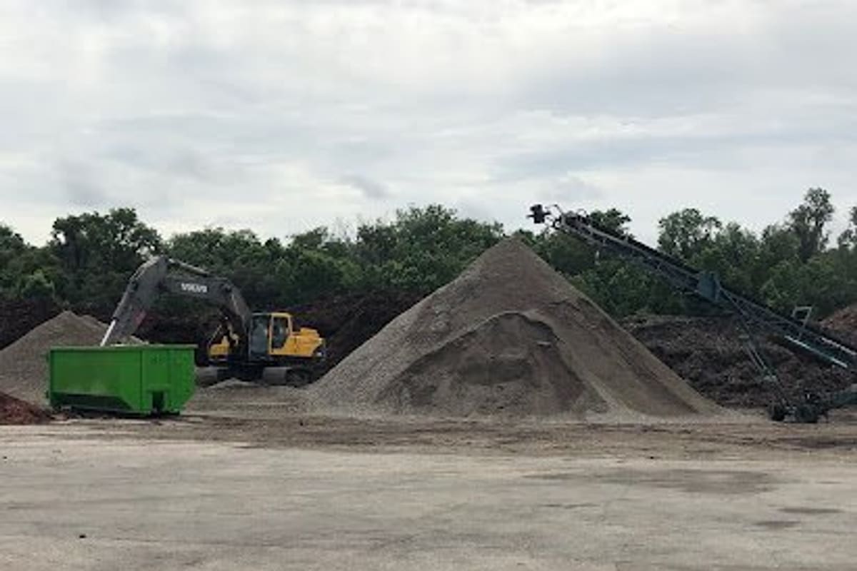 Scrap It In Mulberry: Large gravel and soil piles in an open yard with an excavator, green dumpster and conveyor under a cloudy sky