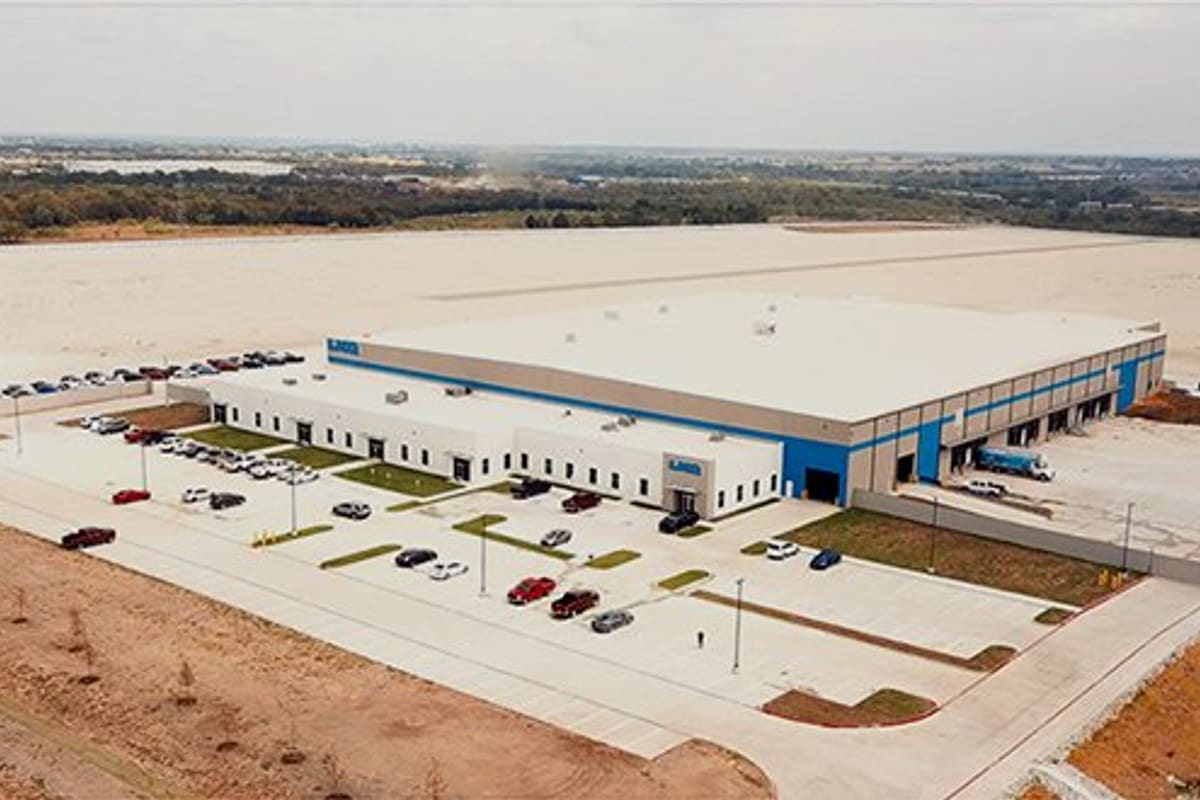 LKQ - Wilmer: Aerial view of a large warehouse facility with loading docks and a parking lot surrounded by cleared land