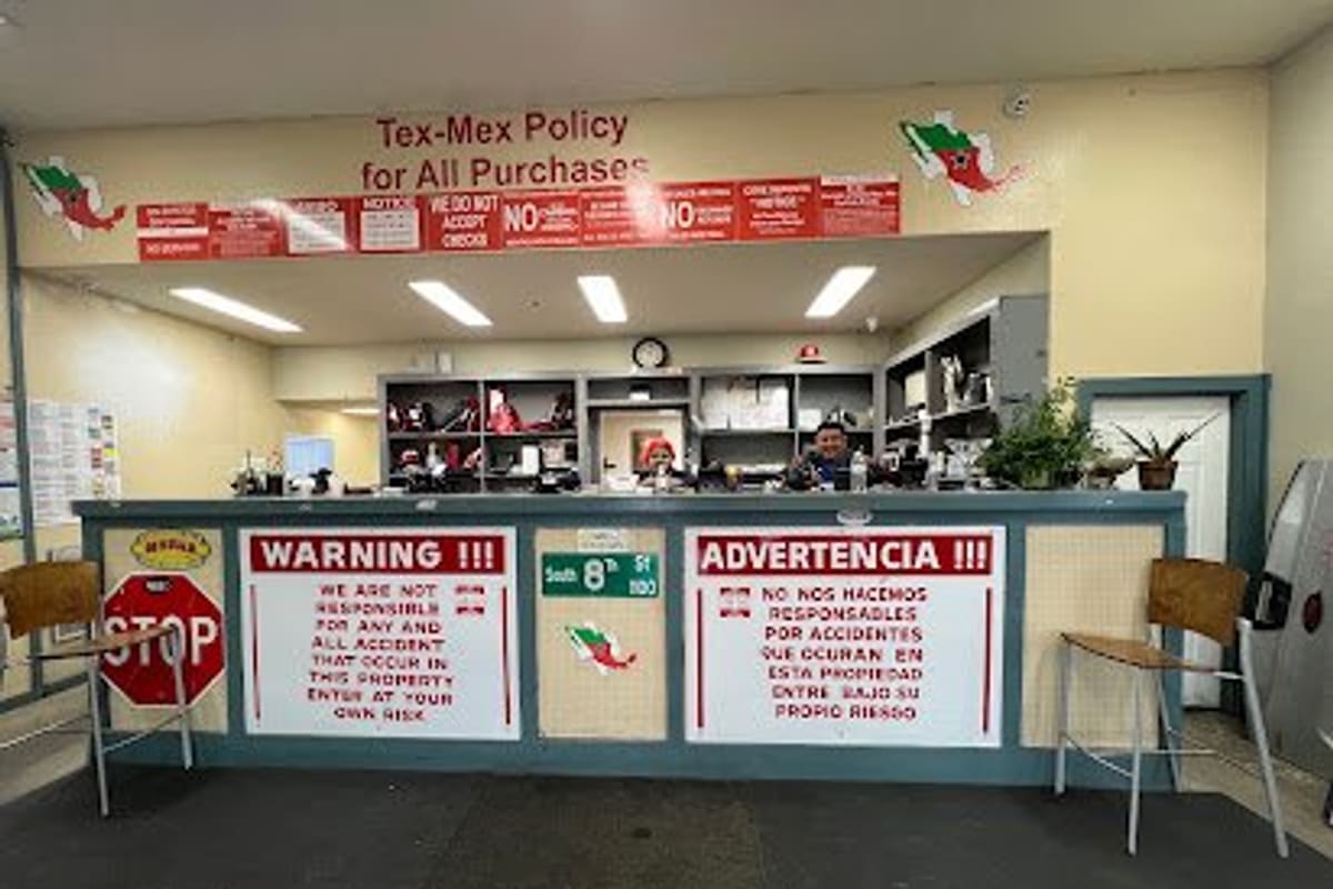 Tex-Mex Auto & Truck Salvage: Indoor sales counter with red warning signs in English and Spanish, shelves behind it, and chairs in front