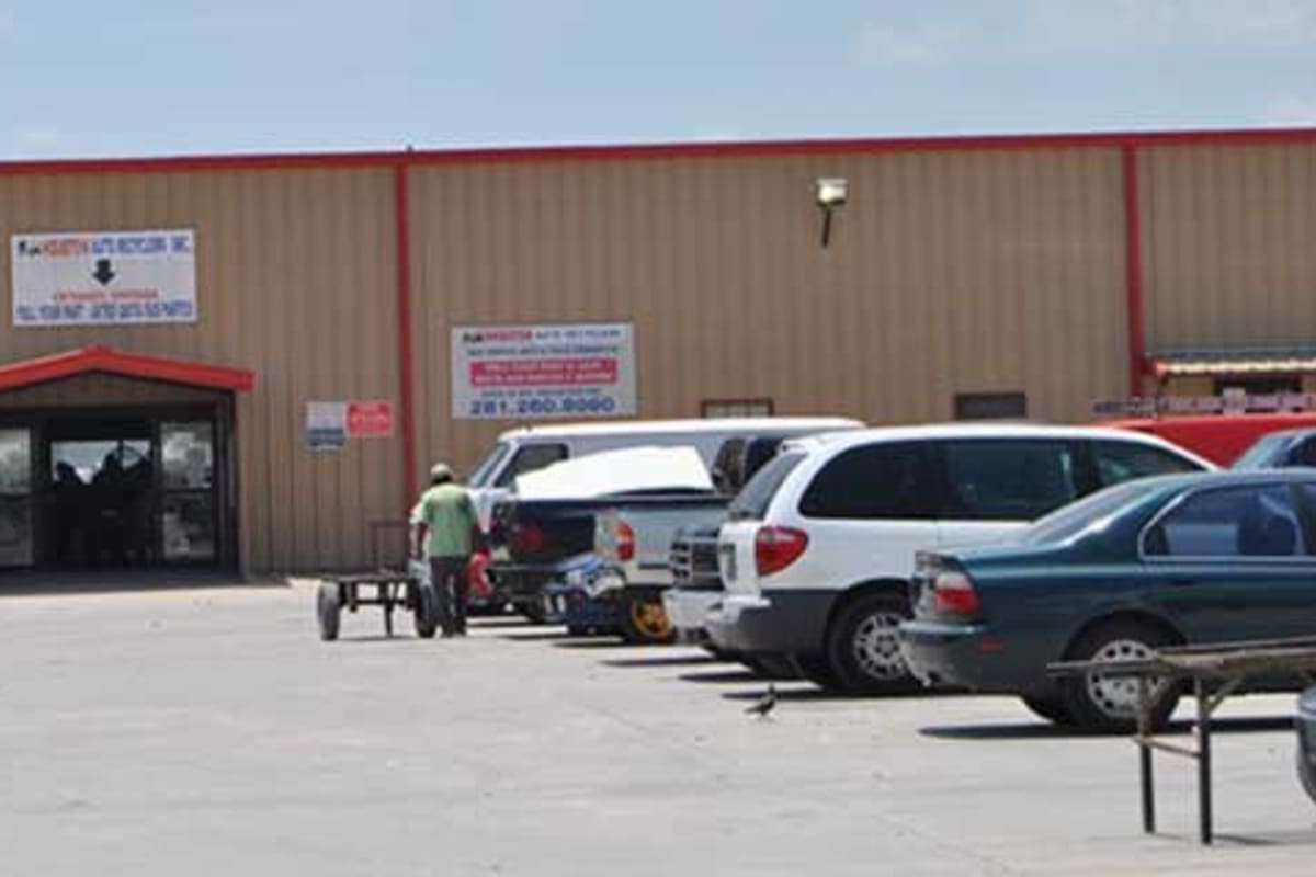 Big-H Auto Recyclers: Tan metal warehouse building with a red-trimmed entrance and signs, and cars parked in the lot in front