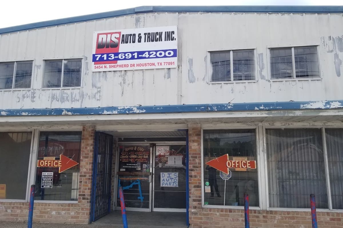 Dis Auto & Truck: Two-story metal and brick building with a large sign, phone number and address, office arrows and a glass entrance door