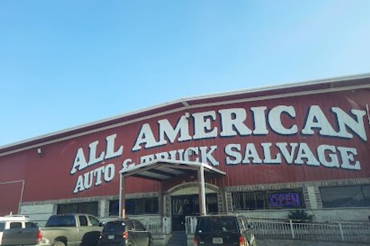 All American Auto Salvage: Large red metal building with big white lettering, a covered entrance, an open sign and parked trucks in front