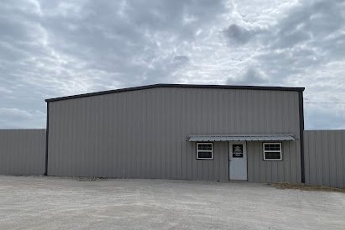 Frontier Auto Parts: Gray metal building with a small awning, two windows and a white door, set behind a gravel lot under a cloudy sky