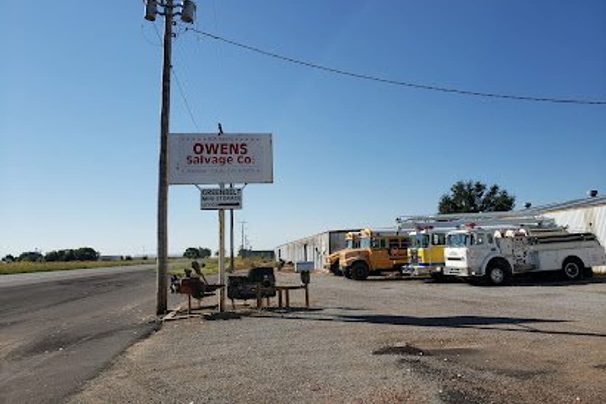Owens Salvage: Roadside sign on a utility pole beside a gravel lot with old school buses and fire trucks parked near a metal building