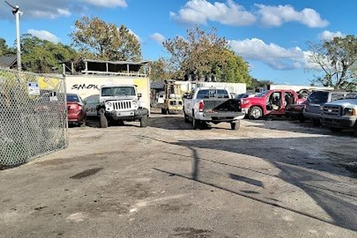 Cuate Services: Wide daytime view of a gravel salvage yard with trucks, a Jeep and other vehicles parked behind chain-link fencing