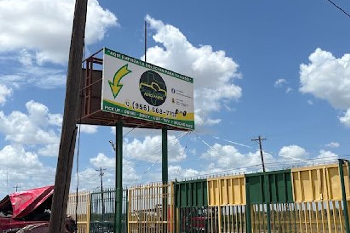 South Jackson Auto Parts: Tall roadside billboard sign on green posts beside a yellow and green gate, with wrecked cars in the foreground