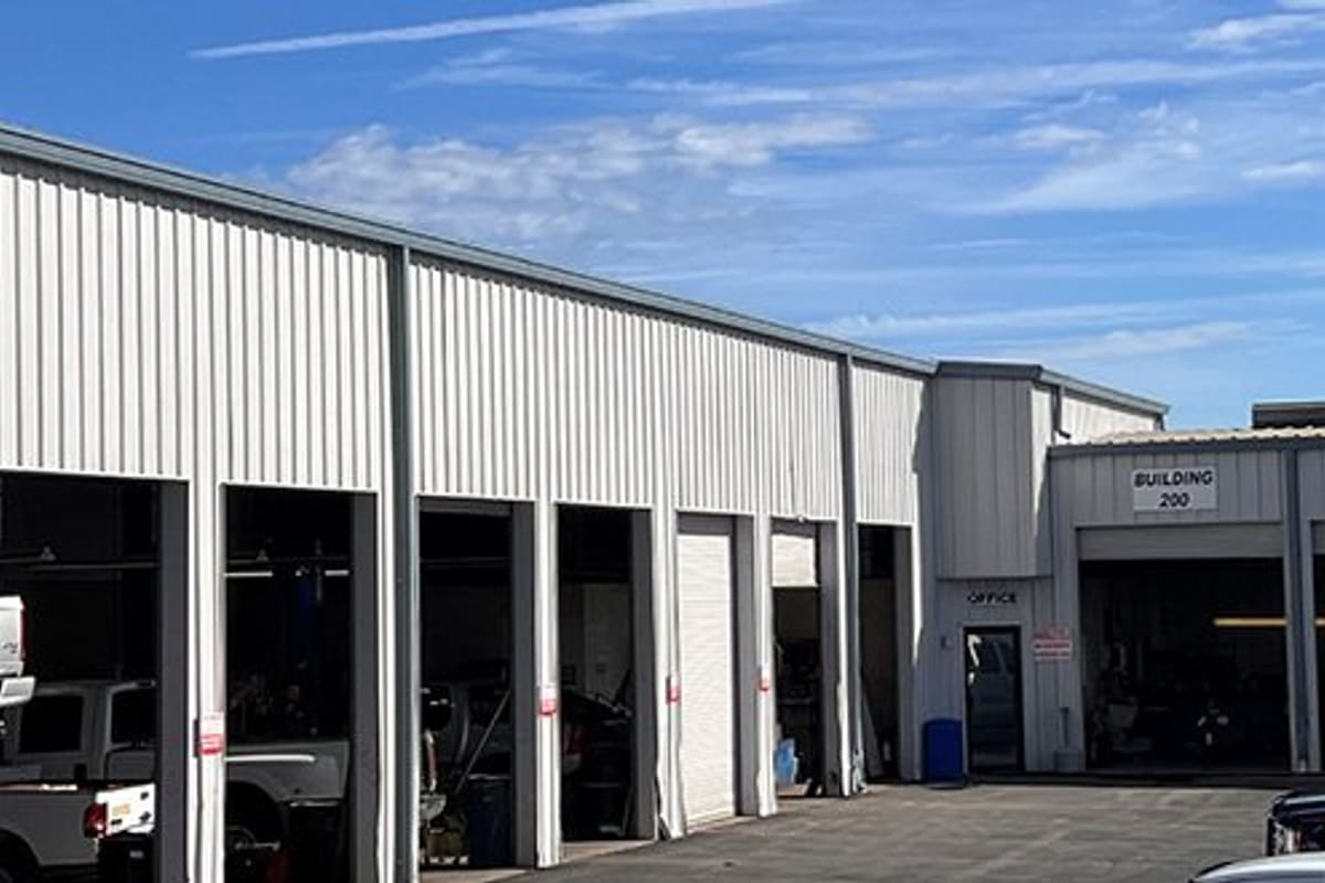 LKQ Crystal River Auto Parts: White metal shop building with open service bays, an office door, and a paved lot under blue sky