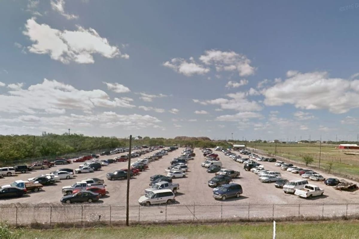 Abilene Police Vehicle Impound: Wide daytime view of a fenced gravel lot filled with rows of parked cars and trucks under a cloudy blue sky