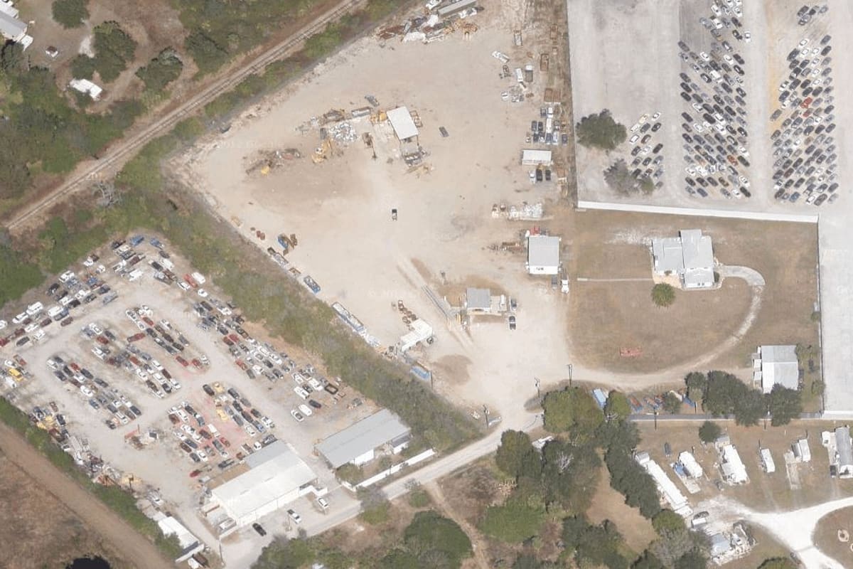 Trademark Metals Recycling: Aerial view of a salvage yard with rows of parked vehicles, dirt lots, and small buildings