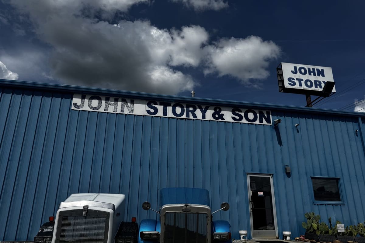 Johns Story Truck Salvage: Blue metal commercial building with large business signs, a glass entrance door, and two truck hoods displayed out front