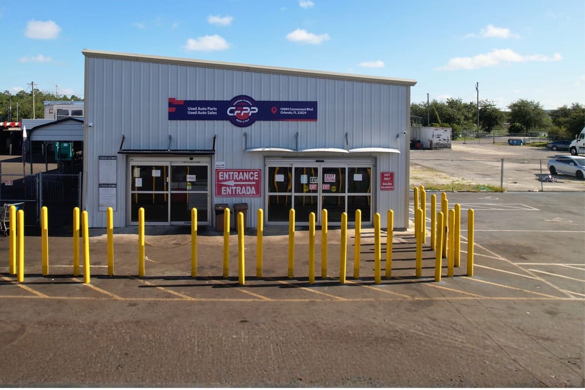 Central Florida Pull & Pay: Metal salvage yard office building with a sign above glass entrance doors and yellow safety posts in front