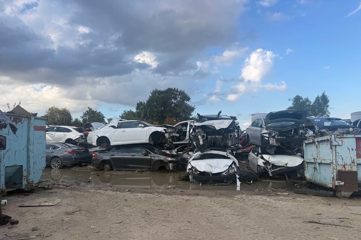 SW Part Zone: Stacked wrecked cars and rusty dumpsters on a muddy salvage lot under a partly cloudy sky
