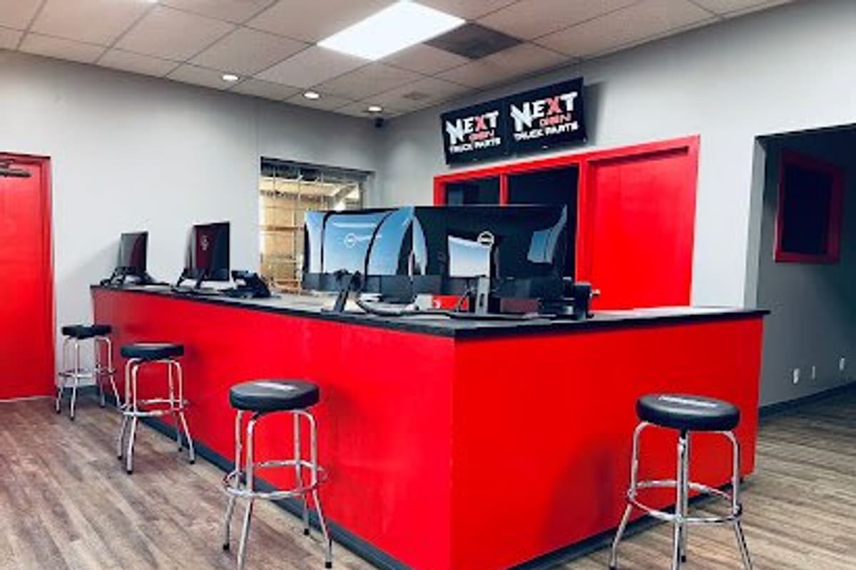 Next Gen Truck Parts: Red service counter with computer monitors and bar stools inside a truck parts store showroom