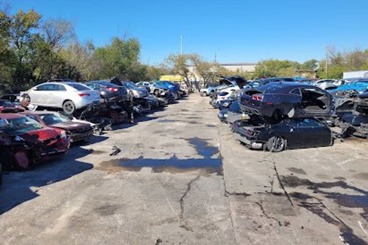 A-Auto Crusher: Wide daytime view of a salvage yard with rows of wrecked and dismantled cars along a cracked paved lane