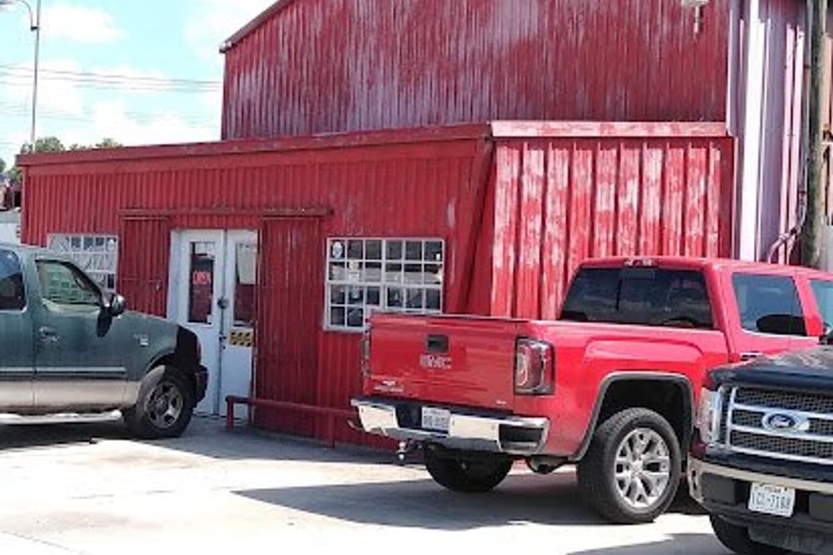 Mittag Auto Salvage: Red metal shop building with a white door and window, with pickup trucks parked in front on a concrete lot