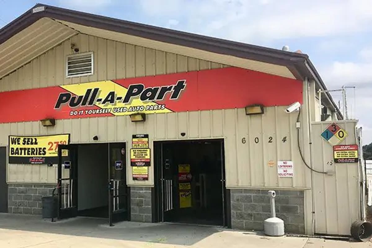 Pull-A-Part Charlotte: Tan metal-sided building with red sign band, open entrance doors, and cars parked to the left