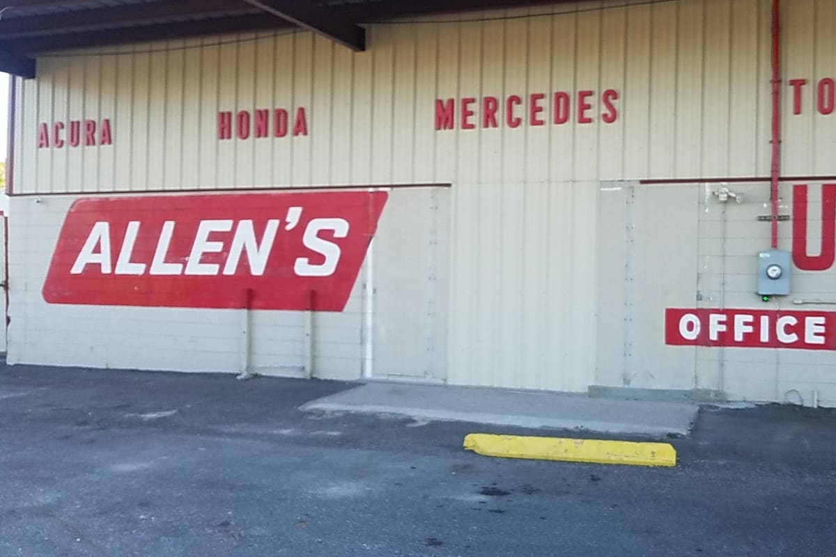 Allen's Used Auto Parts & Cars: Cream metal building with red painted signs listing car brands, a large USED sign and an arrow pointing to the office